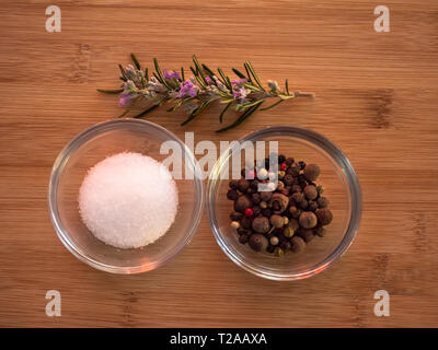 Kristallschalen mit gemeinsamen marine Salz, fünf Pfefferkörner Mix und Rosmarin auf einem Holztisch Stockfoto