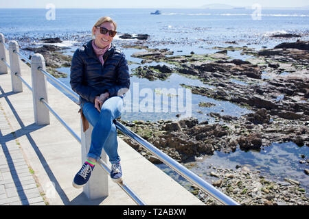 Frau sitzt auf der Reling entlang der Promenade von Sea Point, Kapstadt Stockfoto