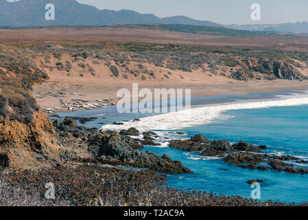 Mit Blick auf die Blue Ocean Waves auf felsigen Ufer rollen mit Dunstige Berge unter dunstig blauen Himmel. Stockfoto