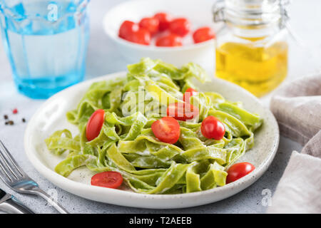 Grüne Spinat Nudeln in Sahnesoße mit Tomaten auf einem Teller. Detailansicht. Leckere Pasta Dinner Stockfoto