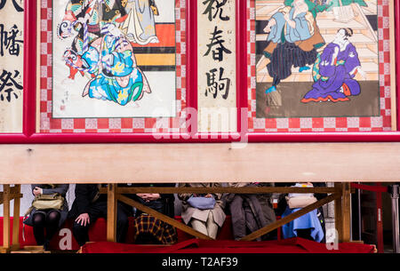 Zeile der Menschen außerhalb Kabuki-za Theater sitzen, Gesichter von Dekorplatten außerhalb Theater, Tokio, Japan verdeckt Stockfoto