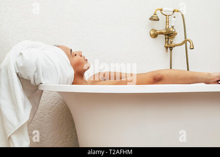 Frau in ein Handtuch um den Kopf entspannen in der Badewanne gewickelt Stockfoto