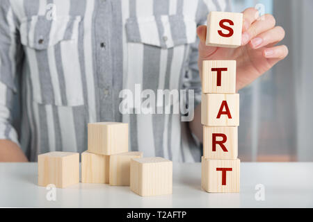 Hand des Weiblichen, Holz Würfel Block mit Worte starten Sie auf dem Tisch. Bis Konzept starten Stockfoto