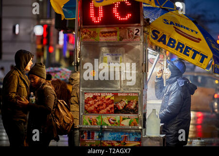 Hot dog street Unternehmer, der von seiner Karre auf 8th Avenue in den dunklen Abend, Manhattan, New York, USA Stockfoto