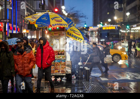 Hot dog street Unternehmer, der von seiner Karre auf 8th Avenue in den dunklen Abend, Manhattan, New York, USA Stockfoto