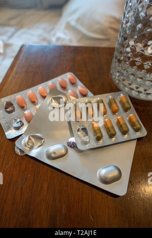 3 Pakete von verschreibungspflichtigen Medikamenten und ein Glas Wasser auf dem Nachttisch Stockfoto