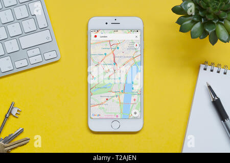 Ein iPhone mit Google Maps Website ruht auf einem gelben Hintergrund Tabelle mit einer Tastatur, Tasten, Notepad und Anlage (nur redaktionelle Nutzung). Stockfoto