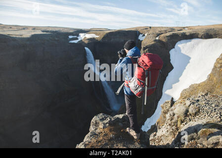 Wanderer mit Rucksack auf einer Klippe mit Wasserfall Haifoss in Island Stockfoto