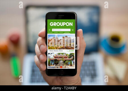 Ein Mann schaut auf seinem iPhone zeigt die Groupon Logo (nur redaktionelle Nutzung). Stockfoto