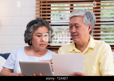 Asiatische senior Paar berechnen Altersvorsorge Finanzdienstleistungen tablet Suche im Dokument auf dem Sofa zu Hause sitzen, Senior lernen Technologie zu verwenden. Altern in Pla Stockfoto