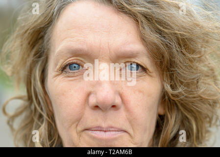Gesicht der Frau mittleren Alters mit blauen Augen, faltiges Gesicht und leicht lockige Haare, an Kamera suchen Stockfoto