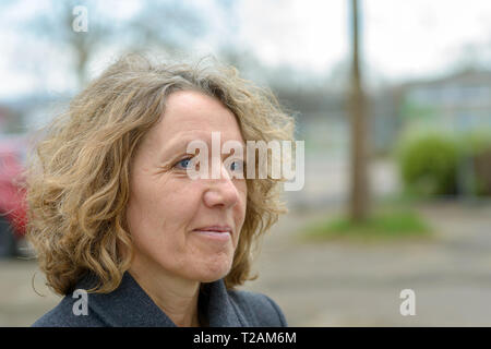 Lächelnd attraktive Frau mit Zerzaustem lockiges Haar einen warmen Wintermantel Stockfoto