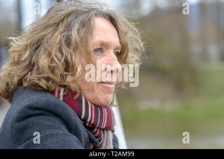 Frau mittleren Alters mit dem lockigen Haar, das Tragen von grauen Mantel und rotem Schal, auf der Brücke stehen, lehnte sich auf Geländer und weg schauen. Close-up Seite Stockfoto