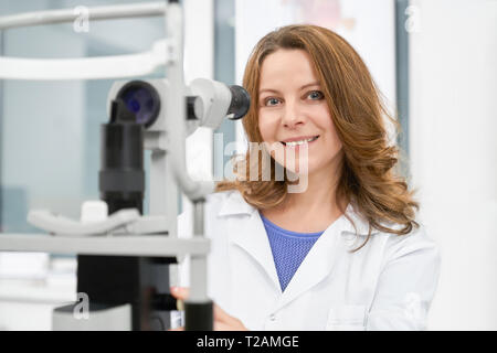 Arzt, Optiker, schöne Frau in der Medizinischen Klinik und die Untersuchung der sehkraft. Augenarzt in weißen Mantel mit optometrie Ausrüstung posiert, s Stockfoto