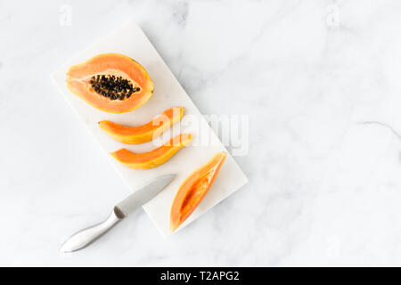 Papaya Hälfte und Scheiben auf weißem Marmor Schneidebrett mit Messer und weißem Marmor Hintergrund mit viel Platz kopieren. Ansicht von oben. Stockfoto