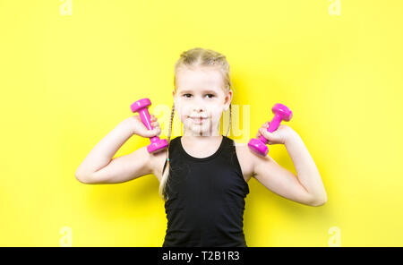 Thema Sport und Gesundheit. Schöne kaukasier kind Mädchen mit Zöpfen auf gelbem Hintergrund mit Smile posieren. wenig Athlet Holding rosa Hanteln. Ba Stockfoto