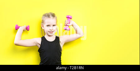 Thema Sport und Gesundheit. Schöne kaukasier kind Mädchen mit Zöpfen auf gelbem Hintergrund mit Smile posieren. wenig Athlet Holding rosa Hanteln. Ba Stockfoto