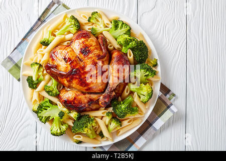 Ansicht des Ganzen gebackenes Huhn mit Brokkoli und Penne Rigate auf einem weißen Teller auf einem rustikalen Holztisch, Ansicht von oben, flatlay, close-up Stockfoto