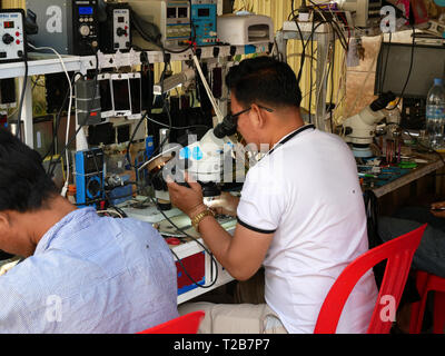 Techniker Reparatur Handys in einem offenen Glasfront und Shop in einem kambodschanischen Marktstadt. In Battambang, Kambodscha 13-12-2018 Stockfoto