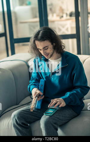 Aufmerksamen jungen Gitarristen mit langen Haaren Holding ein Musikinstrument Stockfoto