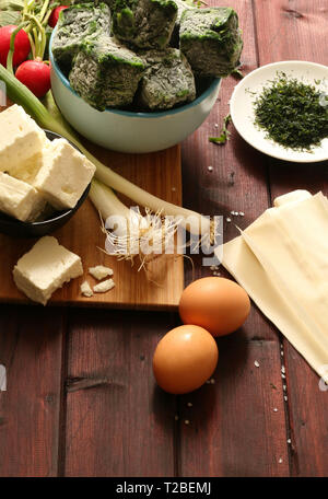Traditionelle griechische Küche. Blick von oben auf die Zutaten für Spanakopita pie mit Spinat und Feta Käse auf dem Holztisch. Stockfoto