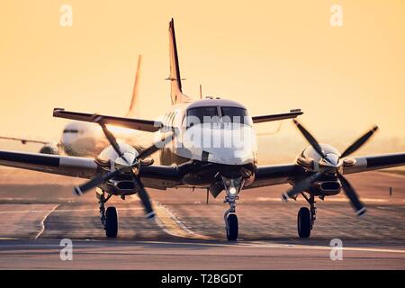 Moderne propeller Flugzeug gegen kommerzielle Flugzeug auf der Landebahn. Verkehr am Flughafen während des Sonnenuntergangs. Stockfoto