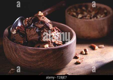 Einstellung Dunkel einer Schokolade Eisbecher mit Soße und Pecan Toppings in eine hölzerne Schüssel Stockfoto