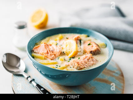 Chowder mit Lachs, Sahne und Kartoffeln in eine blaue Schüssel auf Holztisch. Nahaufnahme Stockfoto