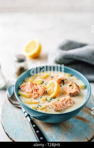 Chowder mit Lachs, Sahne und Kartoffeln in eine blaue Schüssel auf Holztisch. Vertikaler Dampfstoß Stockfoto