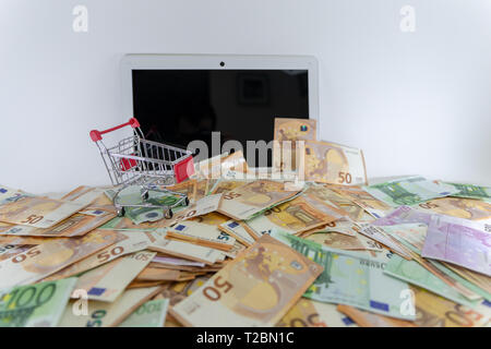 Große Stapel von Euro-banknoten umfasst einen Laptop mit Warenkorb. Online, ecommerce Shopping Konzept. Stockfoto