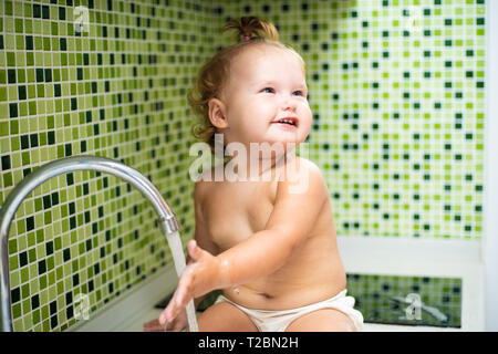 Baby in der Wanne. Baby sitzt in der Küche Spüle und berührte das Wasser aus dem Hahn. baby wäscht seine Hände. Stockfoto