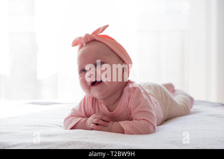 Ein neugeborenes Mädchen mit einem rosa Verband am Kopf ist auf dem Bauch. Das Kind lächelt. Stockfoto