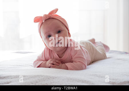 Ein neugeborenes Mädchen mit einem rosa Verband am Kopf ist auf dem Bauch. Das Kind lächelt. Stockfoto