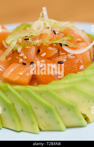 Tartar Lachs Fleisch in Scheiben Avocado gewickelt, garniert mit dünnen Schichten von Lauch, Schwarz und Weiß Sesam auf einer weißen Platte Stockfoto