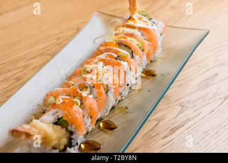 Spezielle Reis Rolle mit Shrimp Tempura, Avocado, Salat, rote Zwiebel, gekochter Lachs, Kaviar, in Scheiben geschnittene Zwiebel und Teriyaki Sauce serviert auf einer Glasplatte Stockfoto