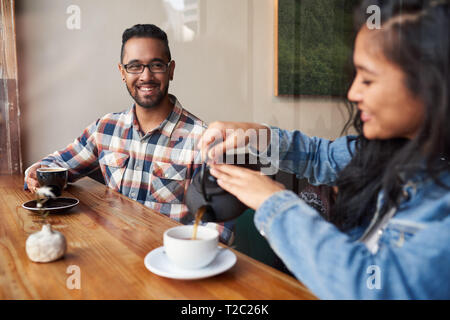 Zwei lächelnde junge Freunde Kaffee trinken und reden, während bei einem Zähler durch das Fenster eines angesagten Cafes sitzen Stockfoto