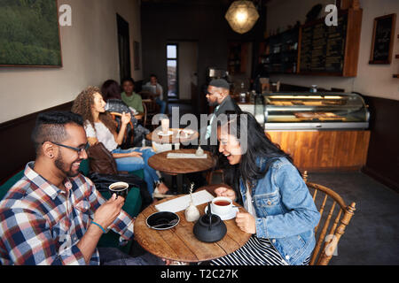 Diverse junge Leute Kaffee trinken und reden, während zusammen an den Tischen sitzen in einem angesagten Cafes Stockfoto
