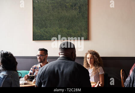 Gruppe von diverse junge Leute zusammen, die an Tischen sitzen in einem angesagten Cafes Kaffee trinken und reden Stockfoto