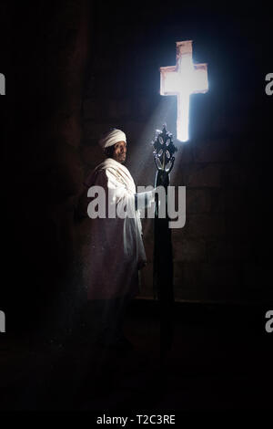 Priester innerhalb einer der Stein Kirchen in Lalibela Äthiopien Holding ein Kreuz Stockfoto