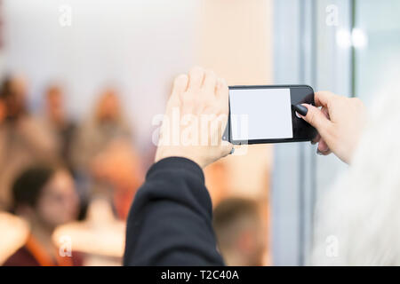 Hände, die mit leeren Bildschirm smartphone en gegen verwackelte Menschen Hintergrund. Stockfoto