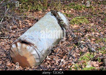 Rusty, verzinkt, zylindrisch, Wassertank in einem grünen Wald Einstellung und zeigt ein rostiges Loch in der kreisförmigen Unterseite aufgegeben. Einsame, verlorene unerwünscht. Stockfoto
