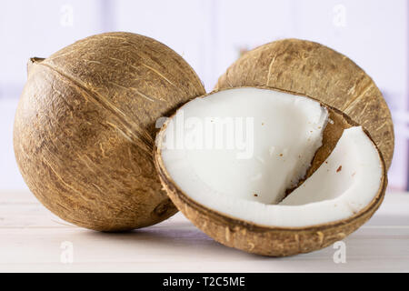 Gruppe von zwei ganze Hälfte der frischen bio Kokosnuss mit roten Blumen in einem weißen Küche Stockfoto