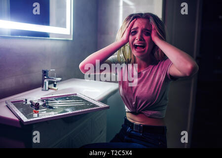 Droge Obsession und Schmerzen. Drogenabhängig hält Hände in die Hand und ist verrückt in der Nähe von Drogen. Drogenabhängige Frau mit Verschmiertem Make-up in der Nacht schreien Stockfoto