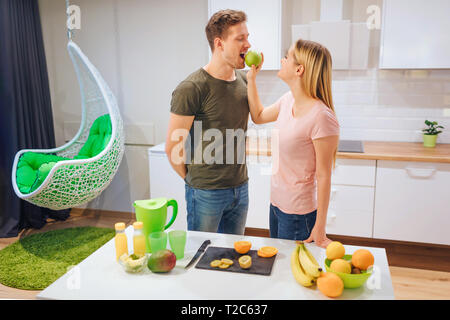 Junge blonde Frau, die ihrem Mann eine organische Apple beim Kochen in der Küche. Das gesunde Essen Familie. Vegetarische Mahlzeit. Diät Entgiftung Stockfoto