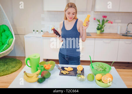 Junge attraktive lächelnde Frau hält frische detox Getränke in Flaschen beim Kochen frische Früchte und Salat in der Küche. Diät detox. Gesunde Ernährung Stockfoto