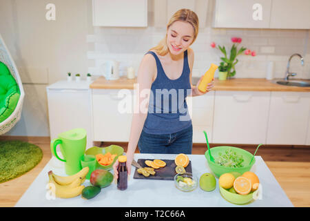 Junge attraktive lächelnde Frau hält frische detox Getränke in Flaschen beim Kochen frische Früchte und Salat in der Küche. Diät detox. Gesunde Ernährung Stockfoto