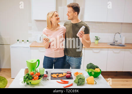 Vegan glücklich liebend Paar hält Flaschen mit natürlichen Smoothie beim Kochen rohes Gemüse in Weiß Küche. Diät detox. Glückliche Familie. Rohkost Stockfoto