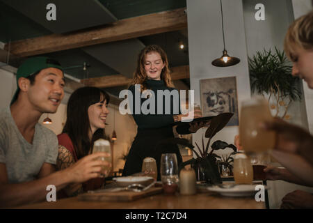 Lächelnde Kellnerin, eine Getränke bestellen zu einer Gruppe von jungen Freunden genießen Sie eine Nacht in einer Bar Stockfoto