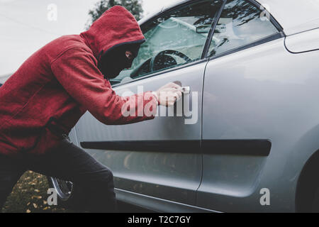 Kriminelle in Schwarz balaclava und Hoodie öffnet jemand das Fahrzeug mit Skeleton Key. Auto brechen durch Unbekannt Männlich mit versteckten Gesicht. Junger Mann nimmt Autom. Stockfoto