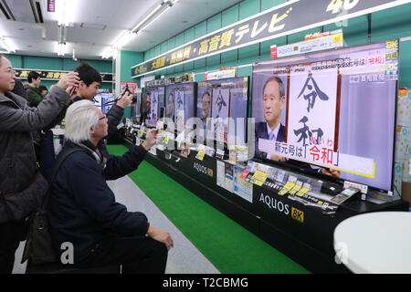 Tokio, Japan. 01 Apr, 2019. Die Menschen sehen eine TV Sendung über Japan's Chief Cabinet Secretary Yoshihide Suga Holding aloft ein gerahmtes Bild von 'Reiwa', der Name des neuen Japan ära, während einer Pressekonferenz in Tokyo, Japan, April 1, 2019. Die japanische Regierung verkündete Montag, 'Reiwa' wird der Name des neuen Japan Ära werden am 1. Mai, als Kronprinz Naruhito steigt die Chrysantheme Thron die Nachfolge seines Vaters Kaiser Akihito zu starten. Quelle: Xinhua/Alamy leben Nachrichten Stockfoto